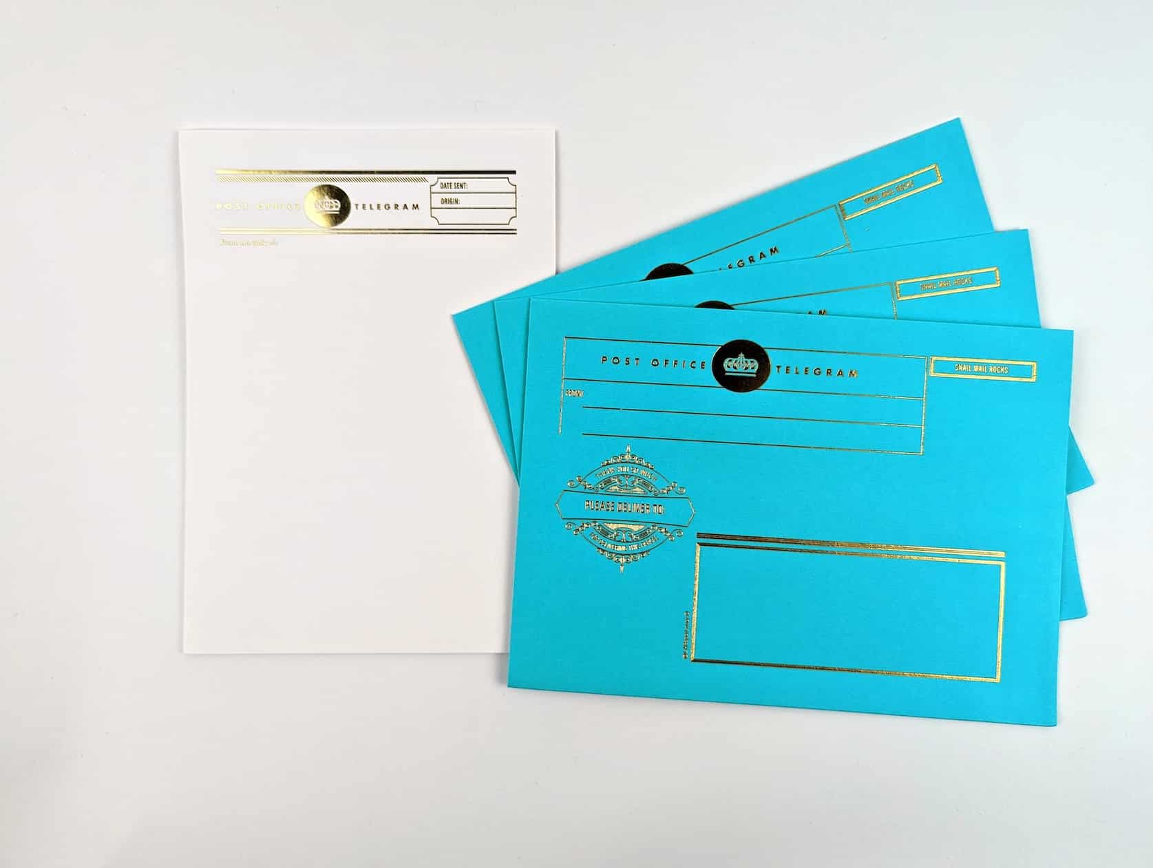 Three turquoise gold foiled envelopes featuring a gold crown, fake postage and text reads: Post Office Telegram. Please Deliver To. Includes white gold foiled letter writing paper in a retro telegram design.