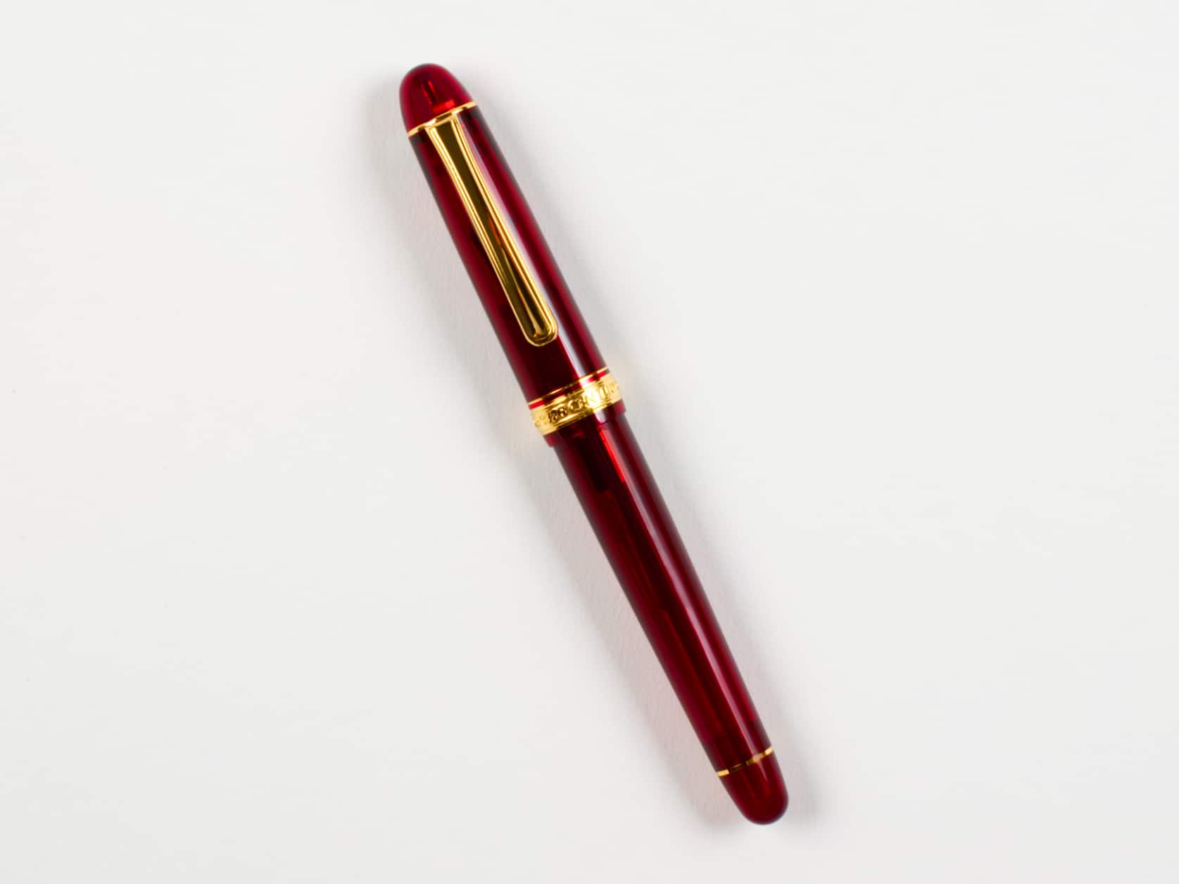 Translucent red fountain pen with a golden clip. Golden ring with embossed pen name at the base of the cap