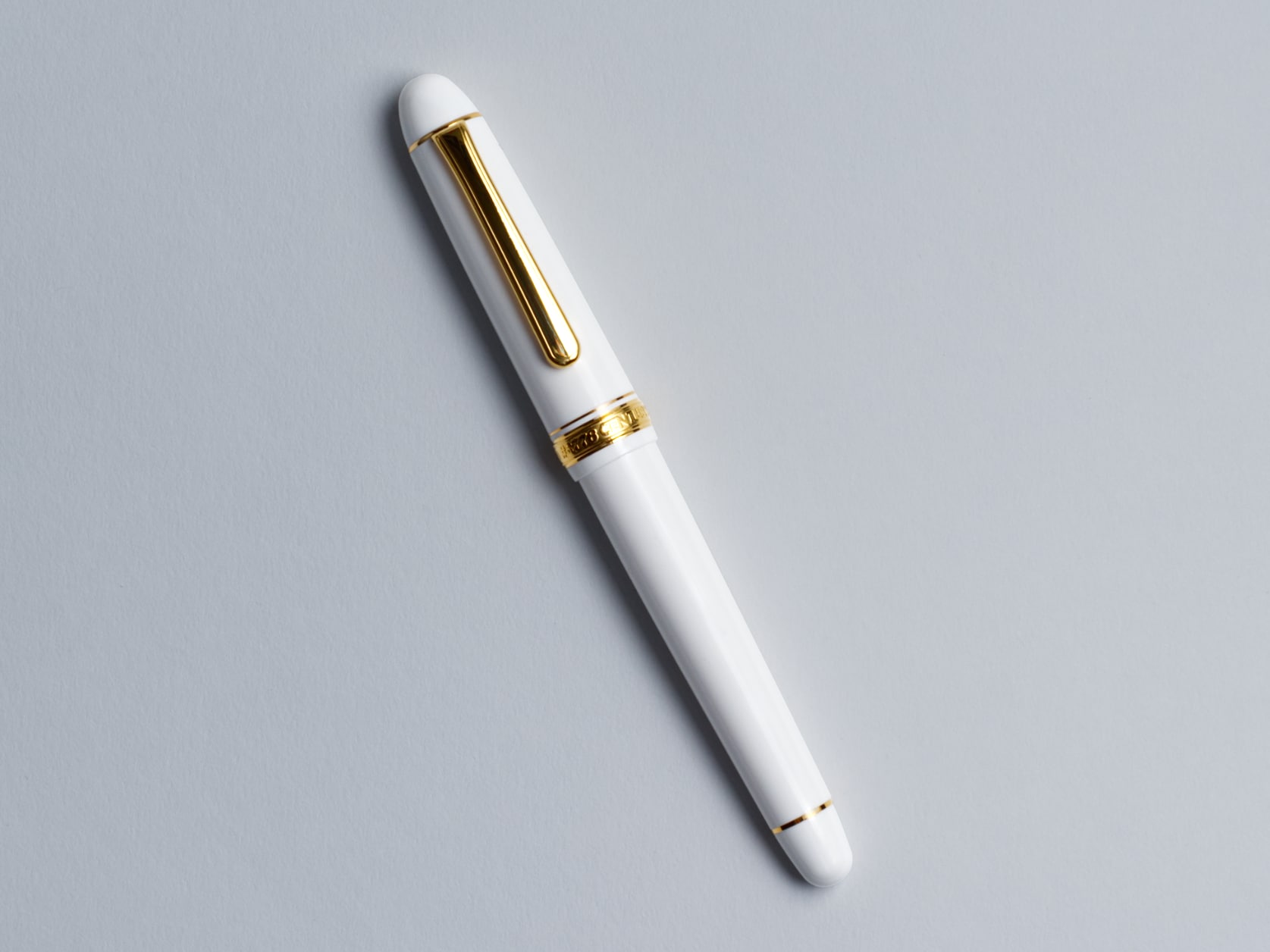 White fountain pen with a golden clip. Golden ring with embossed pen name at the base of the cap