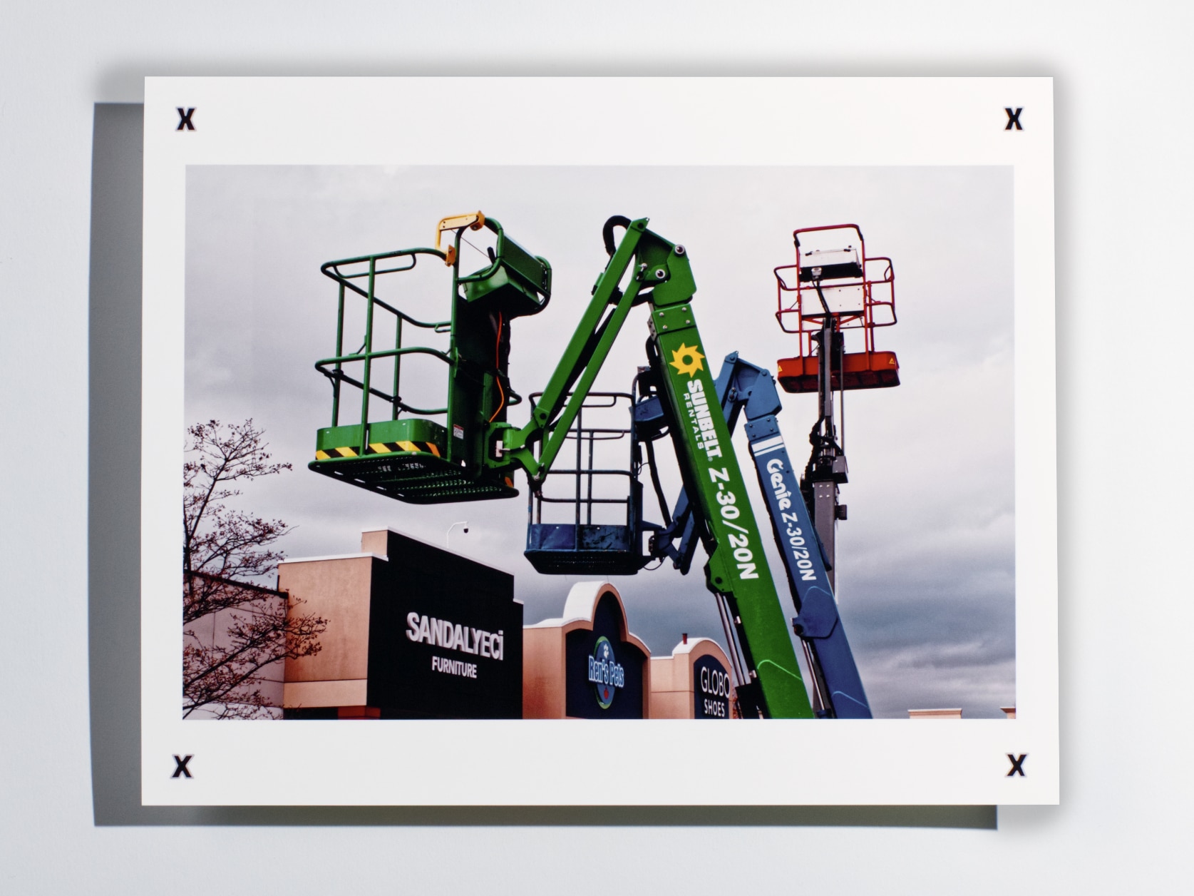 Photography print of 3 man lift cranes in front of a shopping mall on a cloudy day