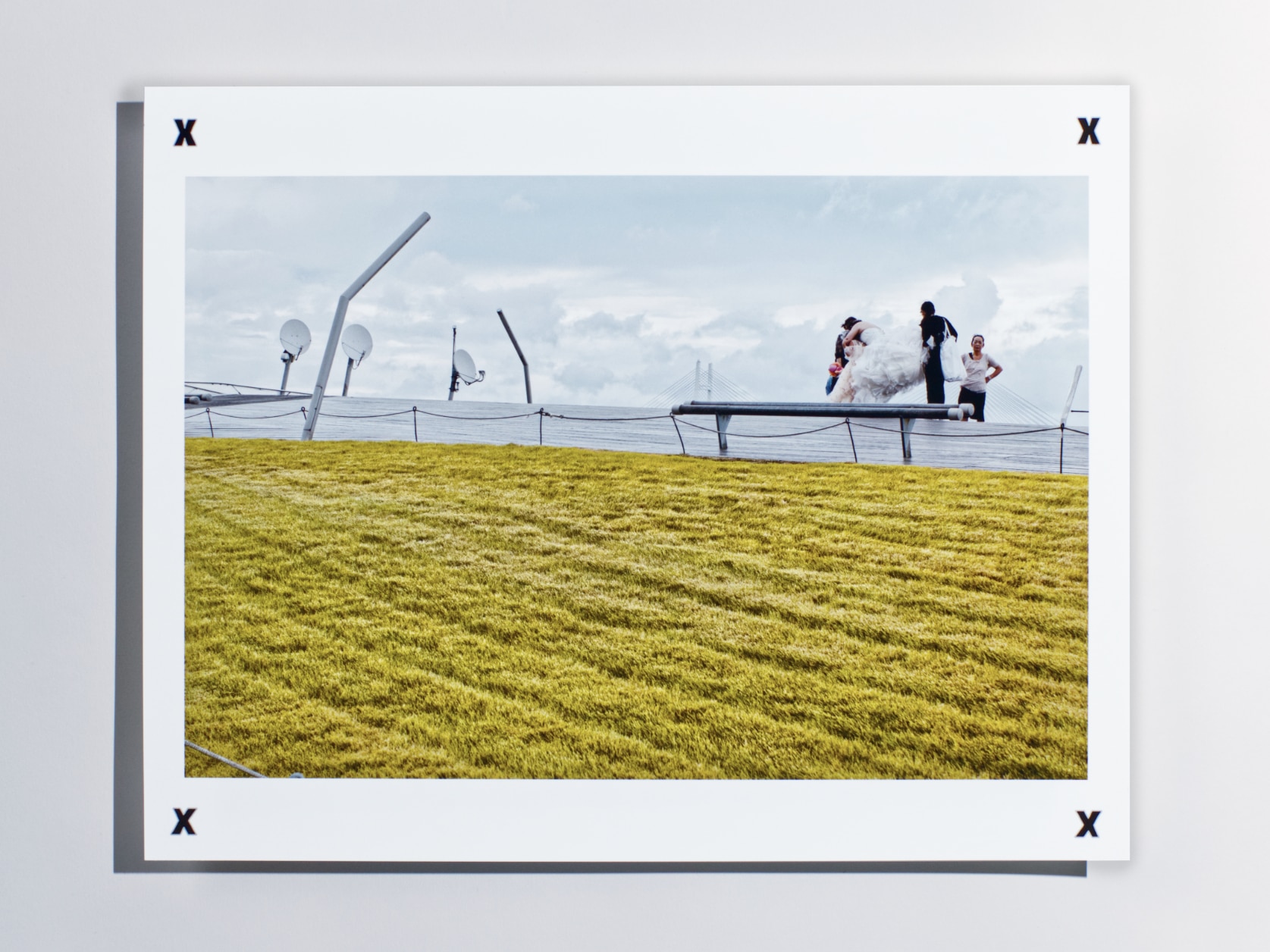 Photography print of people in wedding attire on a wooden pier on a cloudy day. There are satellite dishes and a bridge in the background