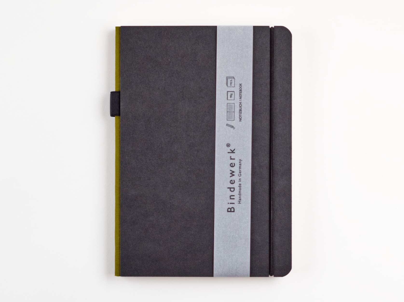 A dark grey notebook with an olive spine, a black elastic and a sleeve with Bindewerk, Handmade in Germany written on it