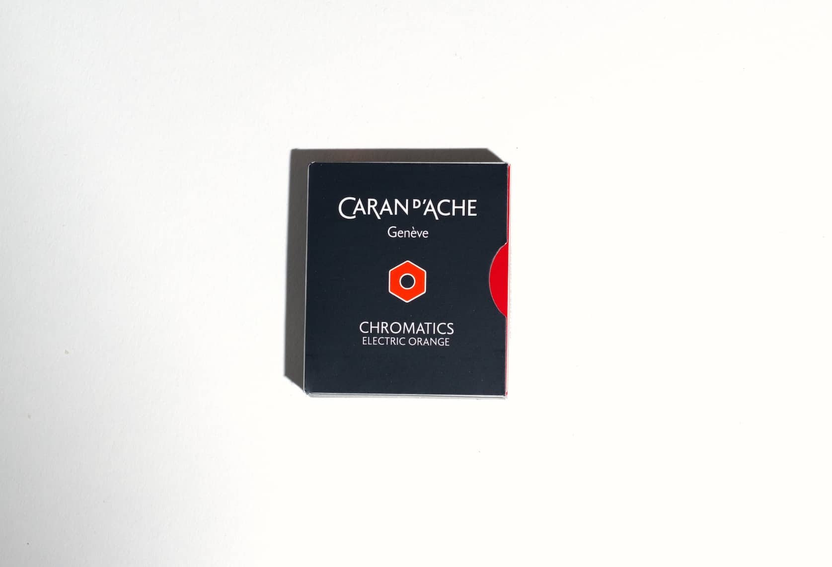 Small black box with a an orange semi circle on the right side. On the front is the Caran d'Ache logo, an orange hexagon. Text reads: Chromatics Electric Orange.