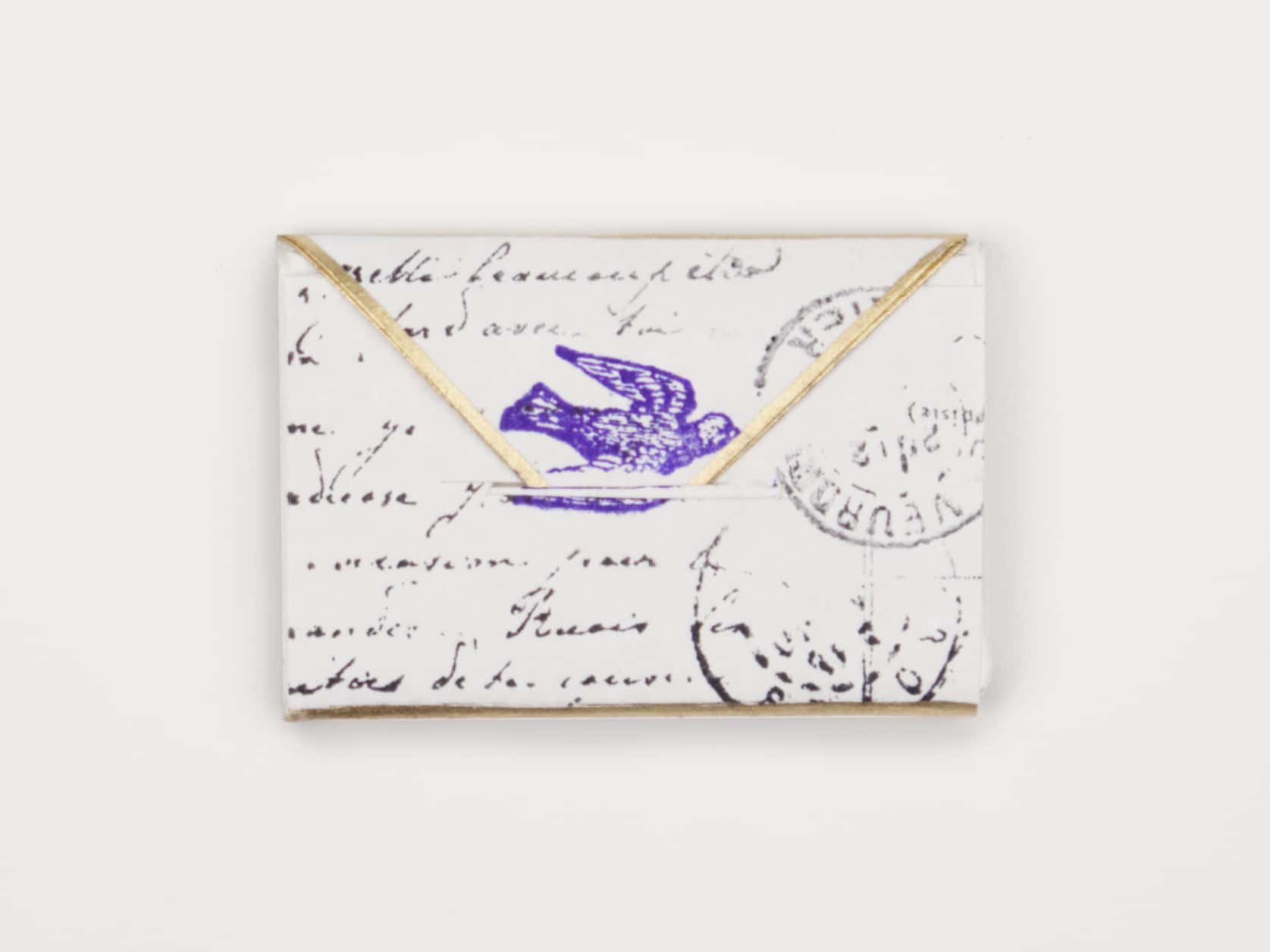 A mini envelope with gold trim on the flap, some writing and stamping on the front and a stamped blue pigeon in the middle.