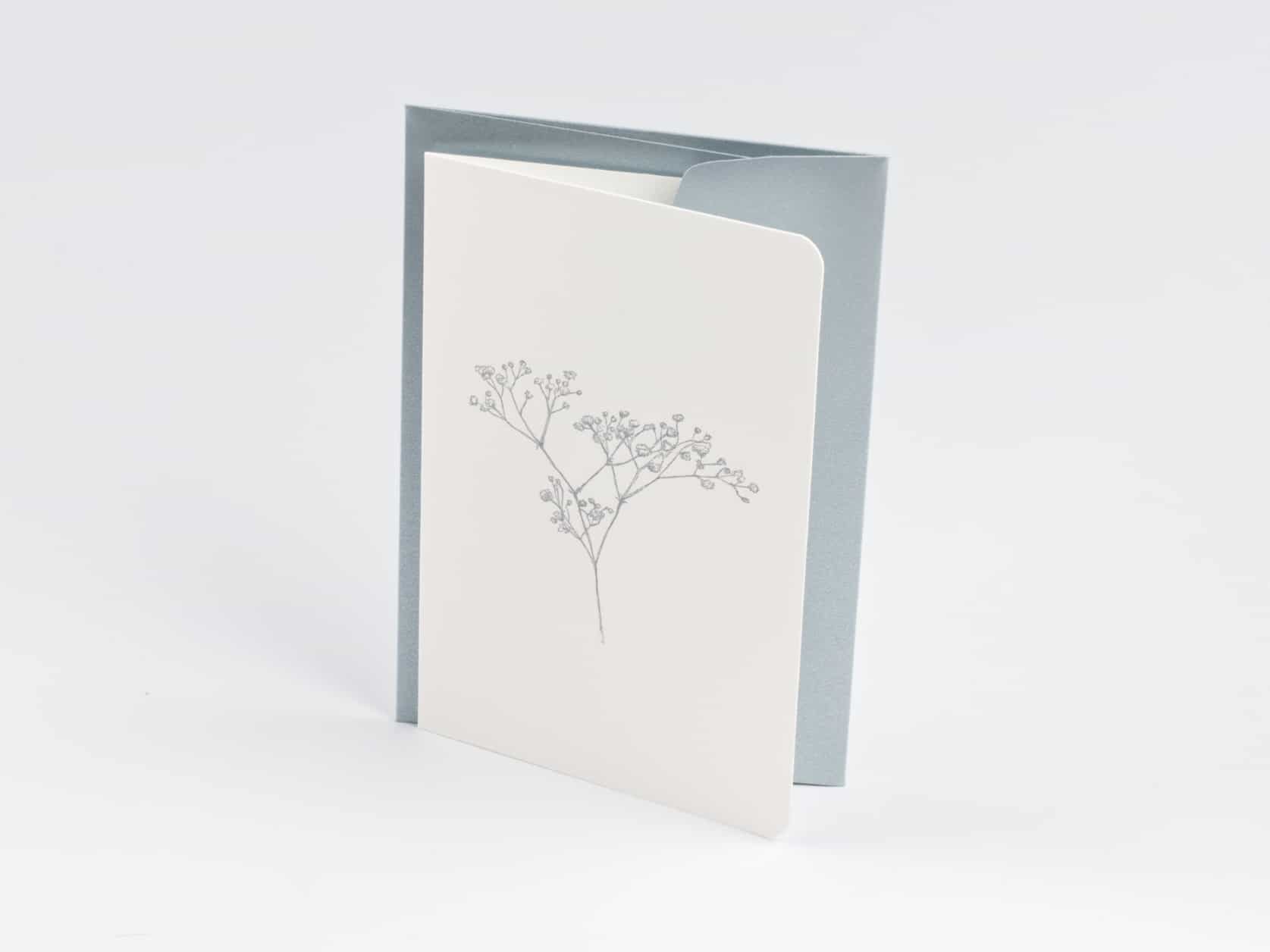 A white card with an illustration of a gypsophile plant on it and a grey envelope standing upright tightly together