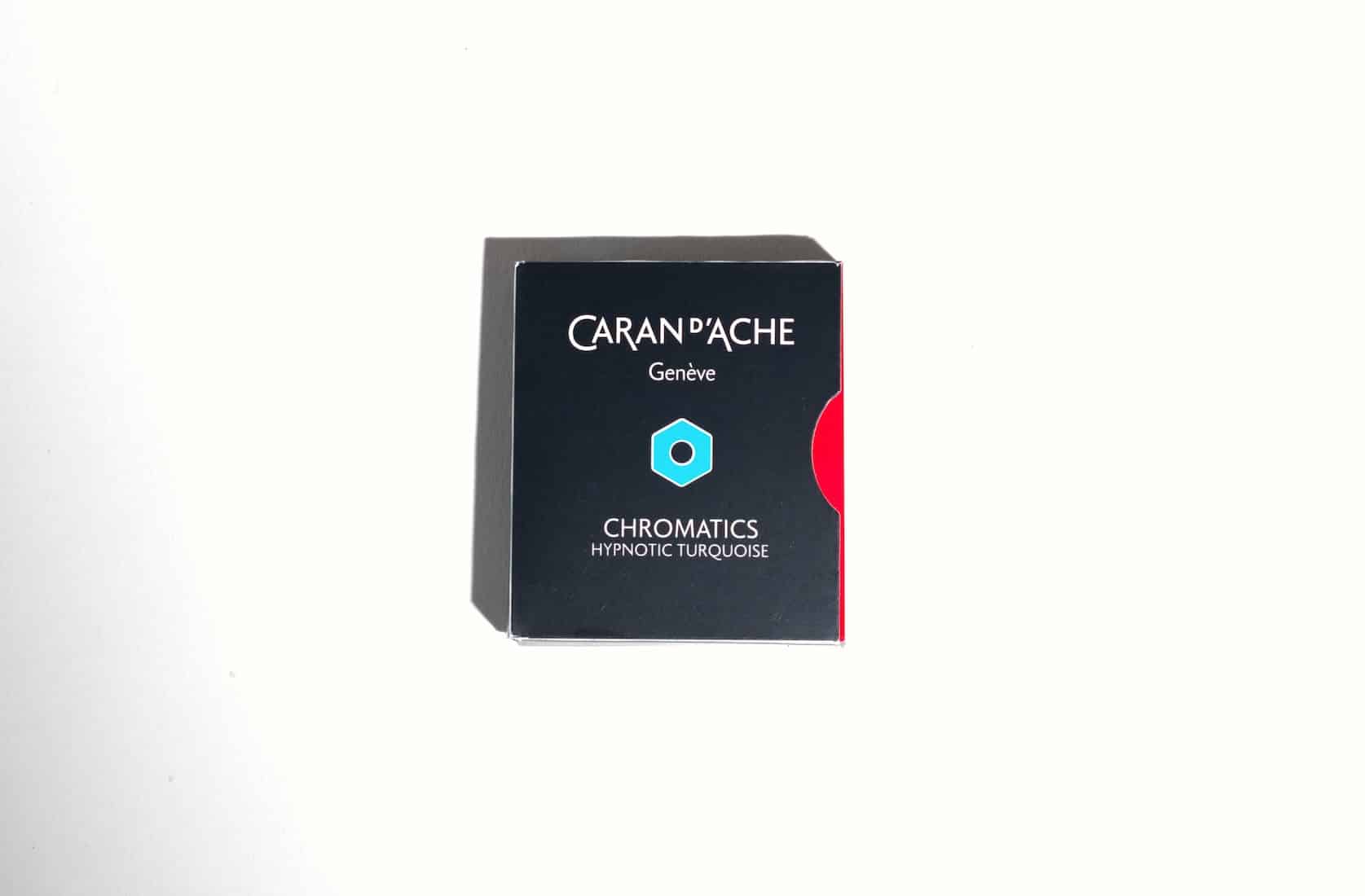 Small black box with a a red semi circle on the right side. On the front is the Caran d'Ache logo, a blue hexagon and text reading: Chromatics Hypnotic Turquoise.