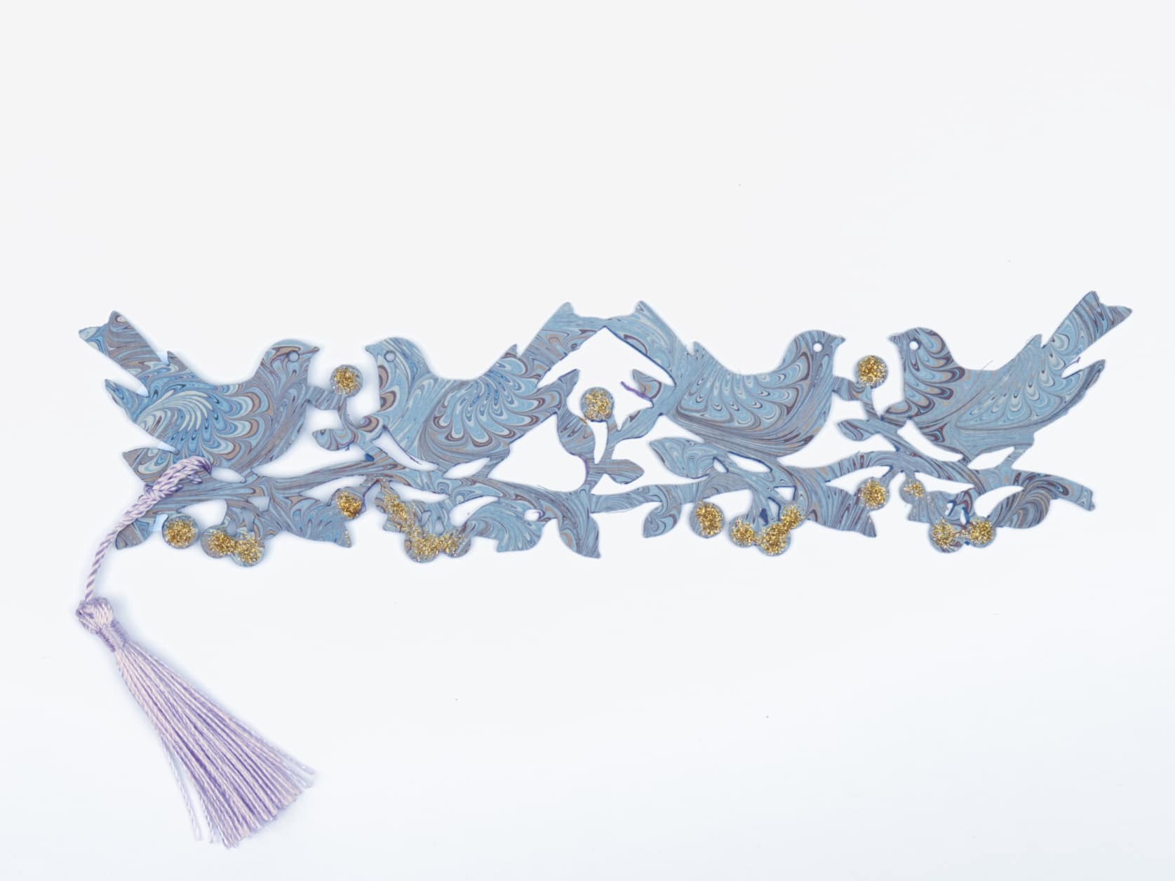 Bookmark consisting of a cutout of four birds on a branch with bulbs coated in gold glitter and a purple tassel on the end. The paper has an intricate blue, white and brown marbled design.