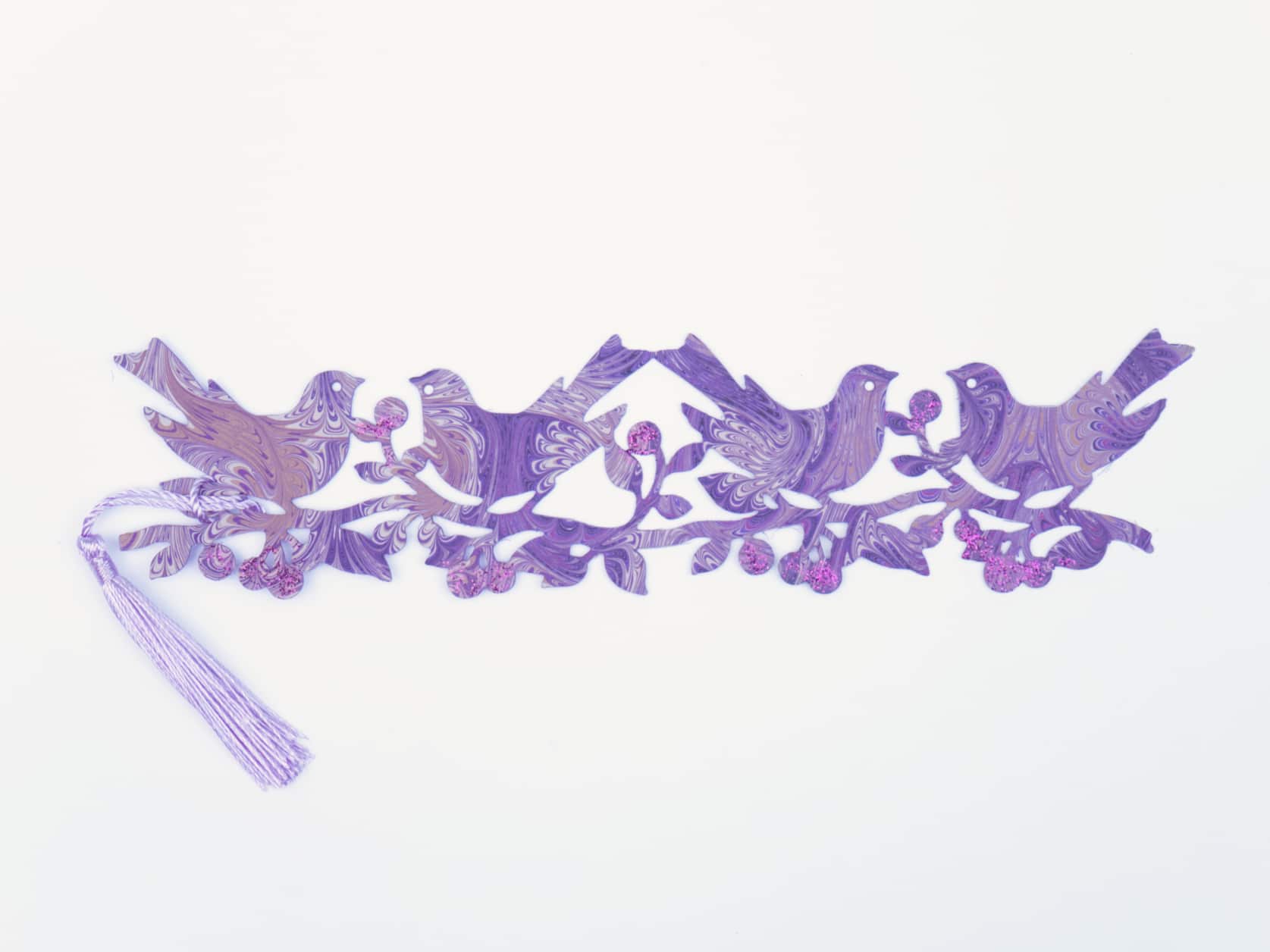 Bookmark consisting of a cutout of four birds on a branch with bulbs coated in purple glitter and a purple tassel on the end. The paper has an intricate purple, white and brown marbled design.