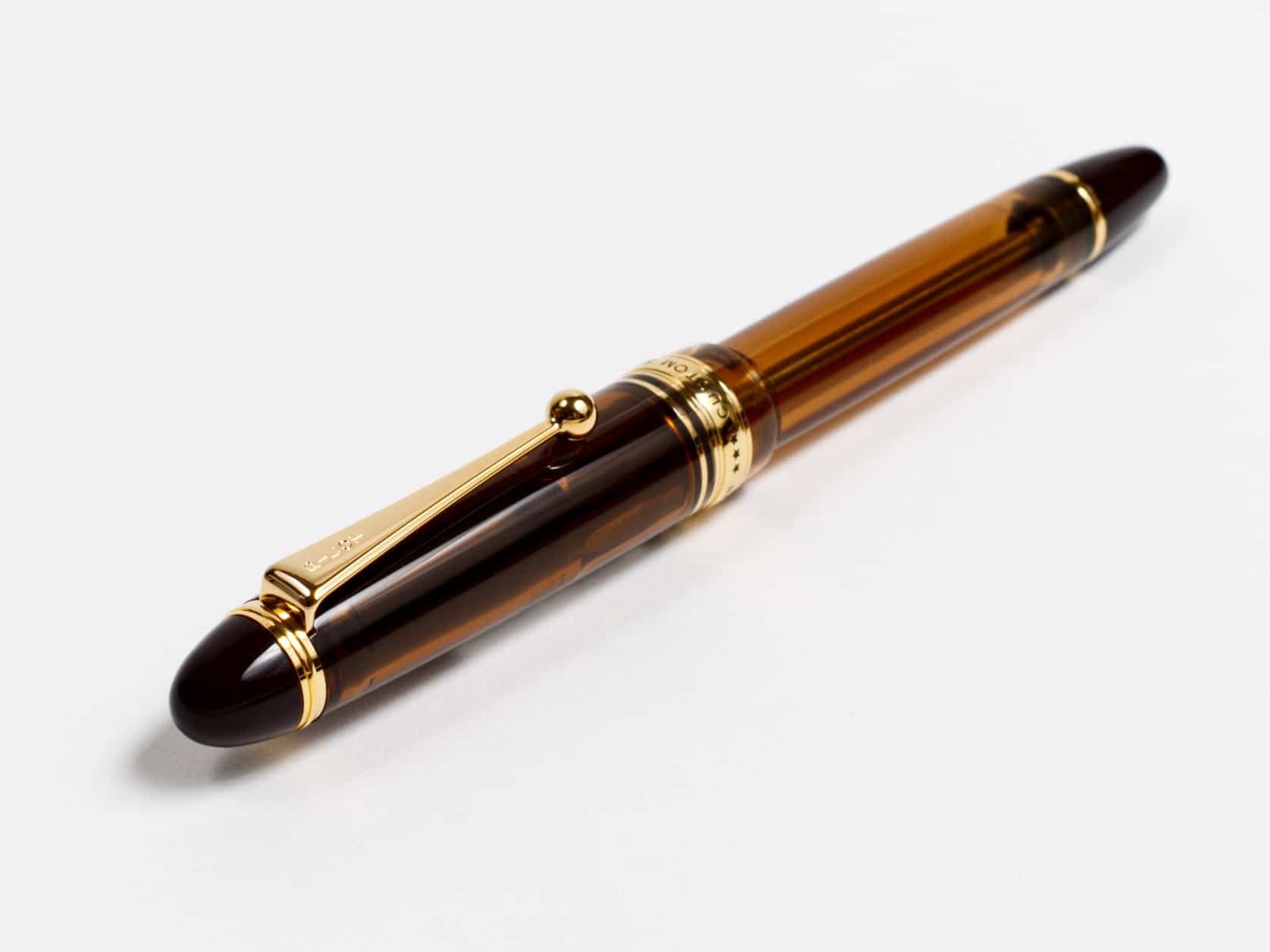 Translucent brown fountain pen with a golden clip and a golden ring around the bottom of the cap