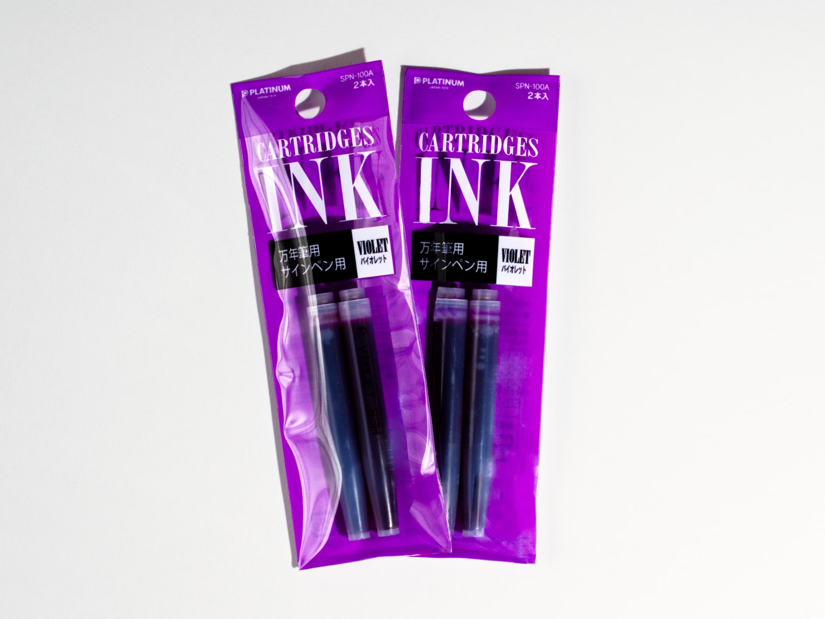 Two purple packs each containing two purple ink cartridges. Text on packs reads: CARTRIDGES INK, Purple.